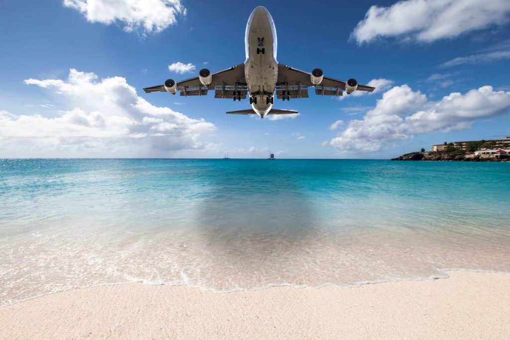 Consigli assicurazione di viaggio, aereo su mare azzurro e spiaggia bianca